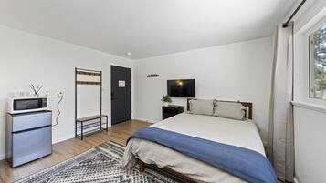 A bedroom with a bed, a TV, a microwave, a refrigerator, and a door with a coat rack.