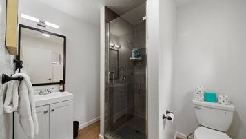 A modern bathroom with a glass-enclosed shower, a white sink, and a toilet.