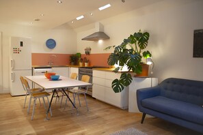 A modern kitchen with white cabinets, a blue sofa, and a dining area with a white table and metal chairs.