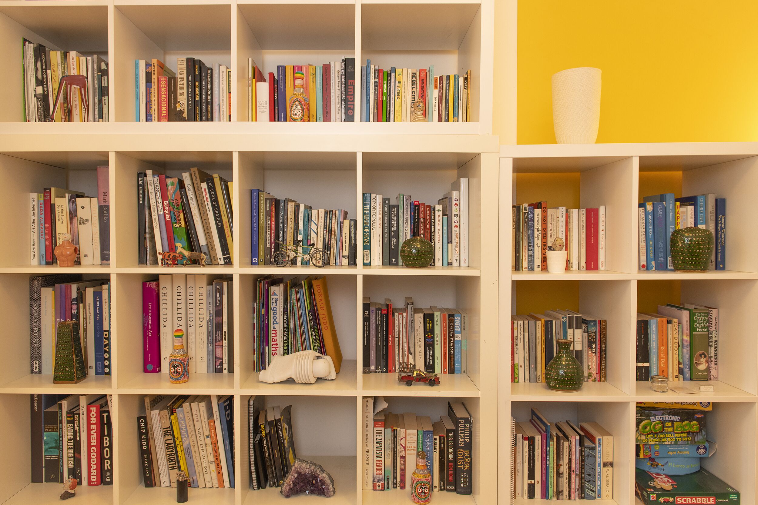 Une bibliothèque remplie de divers livres, dont certains ont des couvertures colorées, ainsi que quelques objets décoratifs, comme une petite figurine et un vase vert.