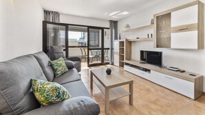 Una sala de estar moderna con un sofá gris, una mesa de centro, un televisor y un balcón con puerta de cristal.