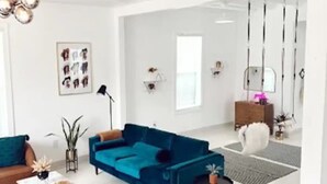 Una sala moderna con un sofá azul, un sillón marrón y una mesa de centro. Hay una planta, una lámpara y un cuadro en la pared.