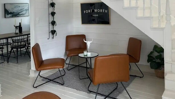 Un interior moderno con una escalera, paredes blancas y un comedor con sillas de cuero.