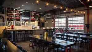 Un restaurante espacioso con techos altos, vigas a la vista y una zona de bar central. Mesas y sillas dispuestas para comer.
