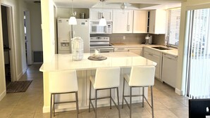 A modern kitchen with a central island, bar stools, stainless steel appliances, and a window with blinds. - Villa Nautica - Perfect for boaters (Cape Coral)