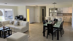 A modern living room with a glass dining table, a sofa, and a kitchen area with white cabinets and appliances. - Villa Nautica - Perfect for boaters (Cape Coral)