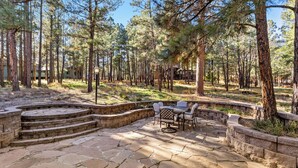 A stone patio with outdoor furniture, surrounded by a forested area. - Slippery Rock Vacation Home - sleeps 9 (Flagstaff)