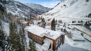 Een modern gebouw met een sneeuwbedekte nok, omgeven door een bergachtig landschap en pijnbomen.