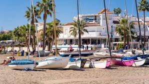 A beach with several boats docked, palm trees, and a building with a tiled roof in the background. - Spectacular Penthouse with panoramic sea views in Riviera del Sol (Mijas-Costa)