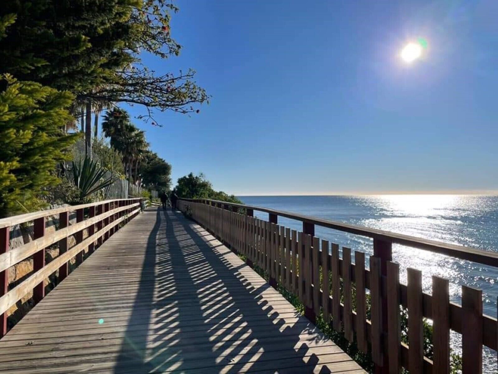 A wooden boardwalk with railings, leading to a body of water.