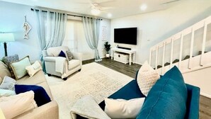 A modern living room with a sofa set, a flat-screen TV, and a staircase.
