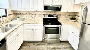 A modern kitchen with white cabinets, a stainless steel refrigerator, a built-in oven, and a microwave.