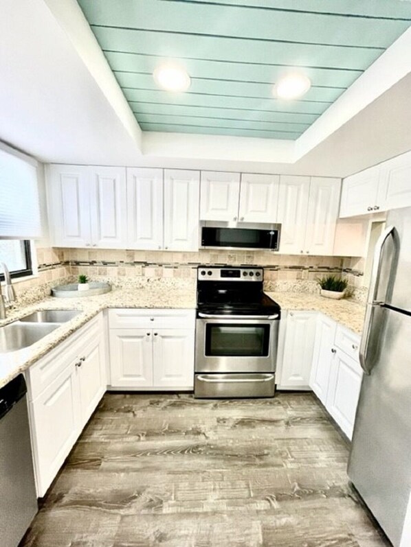 A modern kitchen with white cabinets, a stainless steel refrigerator, a built-in oven, and a microwave.