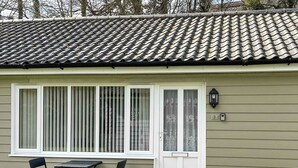 A house with a tiled roof, a front door with a glass panel, a small outdoor table with chairs, and a welcome mat. - A lovely contemporary getaway, just a few steps away from the beautiful beach. (Mundesley)