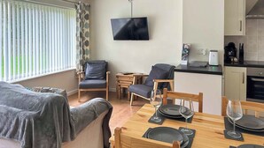 A cozy living area with a sofa, a dining table set for two, and a kitchen area with a coffee machine and a TV. - A lovely contemporary getaway, just a few steps away from the beautiful beach. (Mundesley)