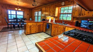 Une cuisine rustique, située dans une cabane en bois, avec un îlot central, un coin repas et de grandes fenêtres.