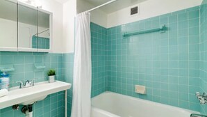 A bathroom with a bathtub, a shower curtain, a sink with a mirror, and a potted plant. - Miami Beach Getaway| Ocean & City Views + FastWiFi (Miami)