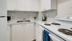 A modern kitchen with white cabinets, a stainless steel sink, a stove, and a microwave. - Miami Beach Getaway| Ocean & City Views + FastWiFi (Miami)
