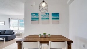 A dining area with a wooden table, white chairs, and three beach-themed wall art pieces. - Miami Beach Getaway| Ocean & City Views + FastWiFi (Miami)