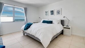 A bedroom with a bed, bedside tables, a window with curtains, and wall art. - Miami Beach Getaway| Ocean & City Views + FastWiFi (Miami)