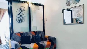 Un divano a tre posti in un soggiorno con pavimento a motivi geometrici, una parete decorata con un simbolo di chiave di violino e un quadro con la scritta “Speranza Fede Amore”.