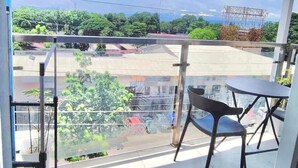 Un balcone con tavolo e sedie, vista su una strada e del verde, e un cielo sereno.