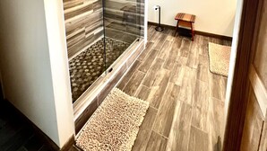 A modern bathroom with a glass-enclosed shower, a wooden floor, and a small bench. - Three-bedroom house with views, decks, golf cart and home gym! (Ocracoke)