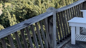 A wooden deck with a white table and chairs, overlooking a forested landscape. - Three-bedroom house with views, decks, golf cart and home gym! (Ocracoke)