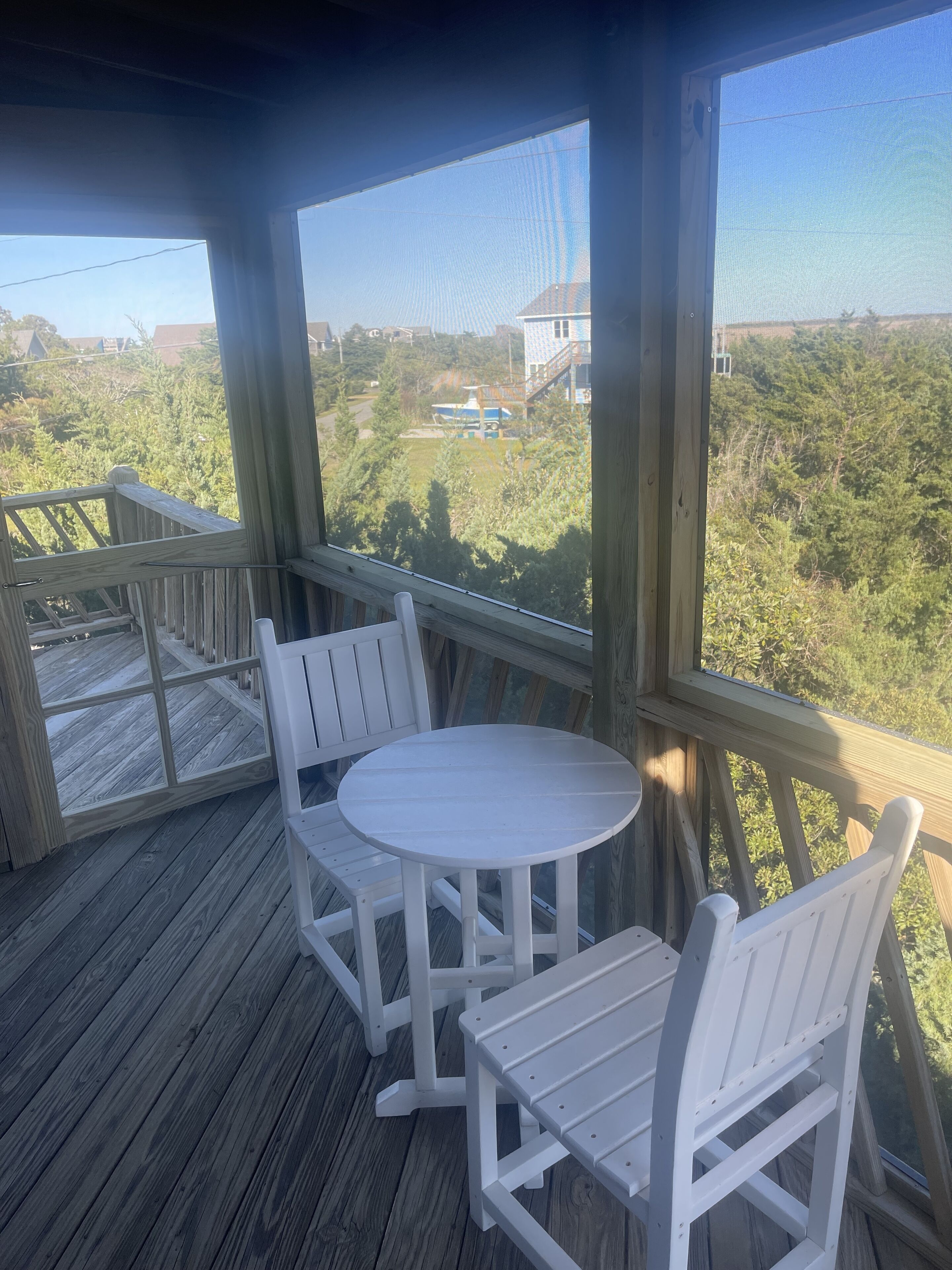A covered outdoor seating area with a round table and two chairs, overlooking a residential area with houses and trees.