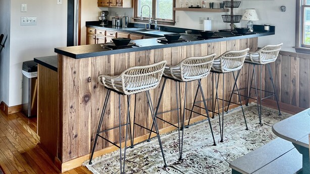 A modern kitchen with wooden ceiling beams, a central island with bar stools, and a built-in oven. - Three-bedroom house with views, decks, golf cart and home gym! (Ocracoke)