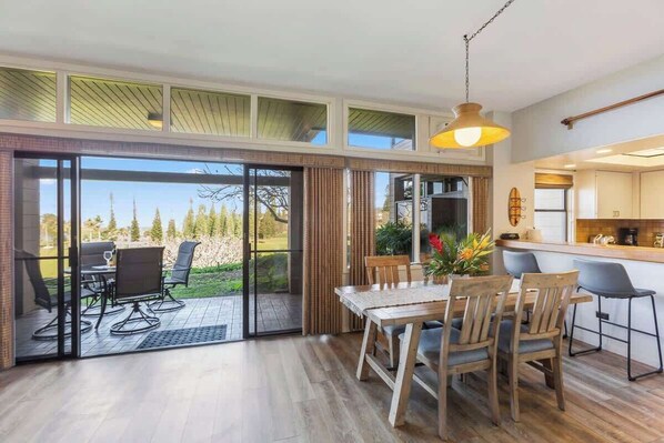 Une cuisine moderne dotée d’un coin bar, d’un espace repas avec une table et des chaises, et d’une porte-fenêtre coulissante donnant sur une terrasse aménagée avec du mobilier d’extérieur.