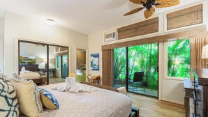 Une chambre d’hôtel avec un grand lit, un ventilateur de plafond, une porte-fenêtre coulissante donnant sur un balcon et une vue sur la verdure environnante.