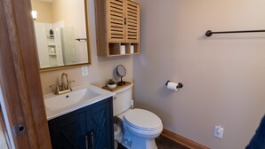 Une salle de bain avec un lavabo blanc, des meubles de rangement bleu foncé, un meuble à pharmacie en bois, des toilettes et un porte-serviettes.
