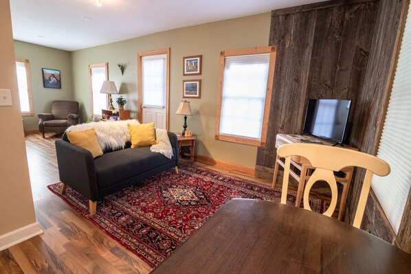 A living room with a dark-colored sofa, a wooden dining table, and a TV on a stand.