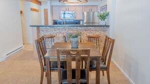 A modern kitchen with a central island, wooden chairs, and a hanging light fixture.