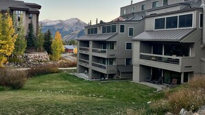 A modern multi-story building with balconies and large windows, set against a backdrop of mountains and autumn trees.