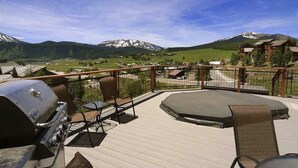 A deck with outdoor furniture, a grill, and a view of mountains.