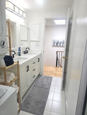 Une salle de bain moderne avec un meuble-lavabo blanc, un miroir, un porte-serviettes et un espace douche.