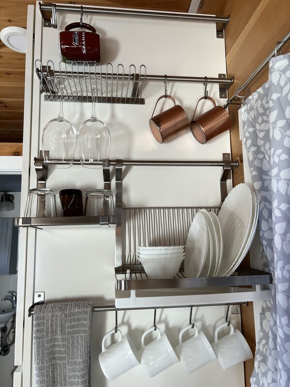 A kitchen with a hanging rack for mugs and glasses, a coffee maker, and a towel rack. - Tacoma Tiny House (Tacoma)