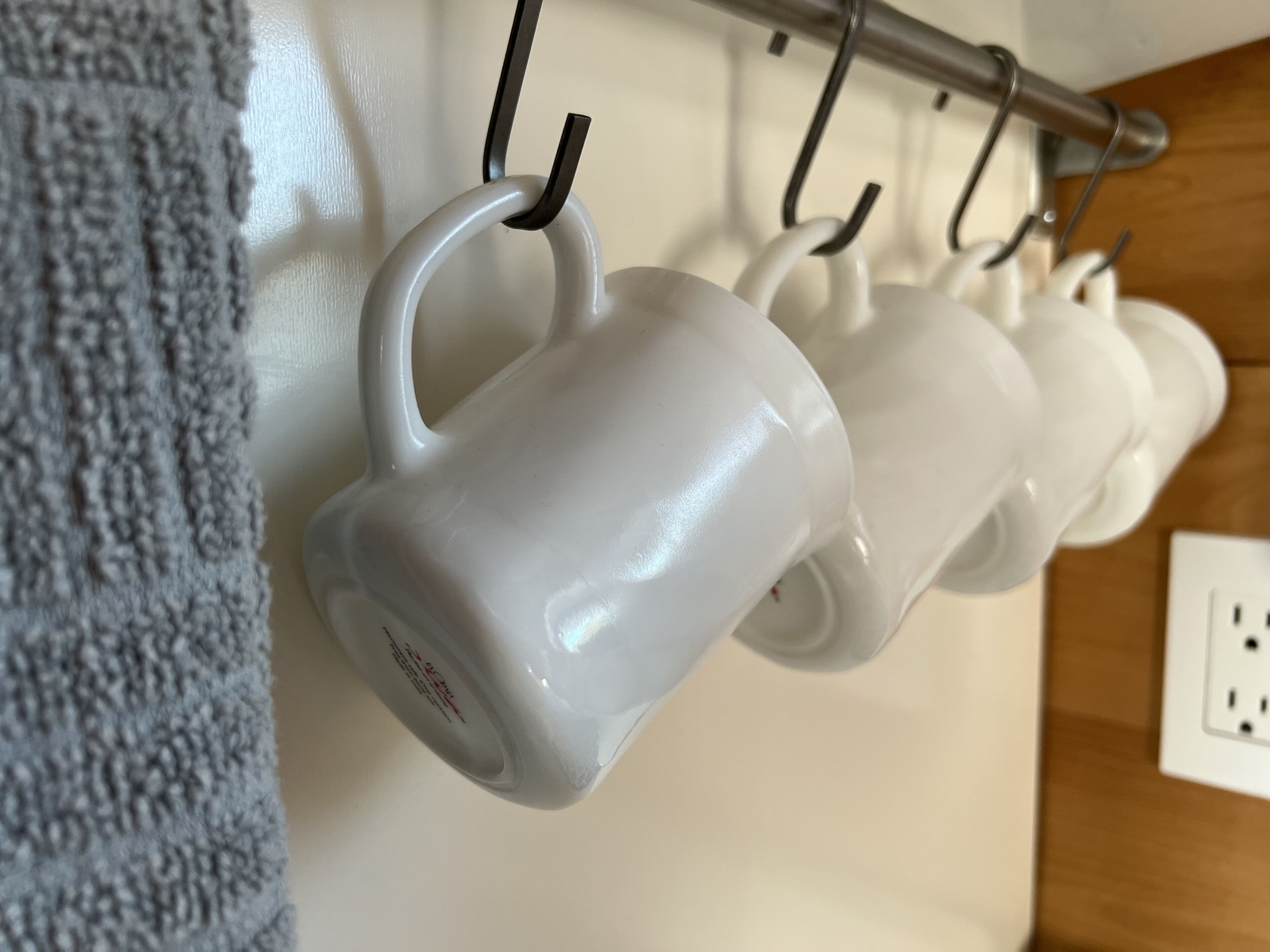 Una hilera de tazas blancas colgadas en un porta tazas metálico.