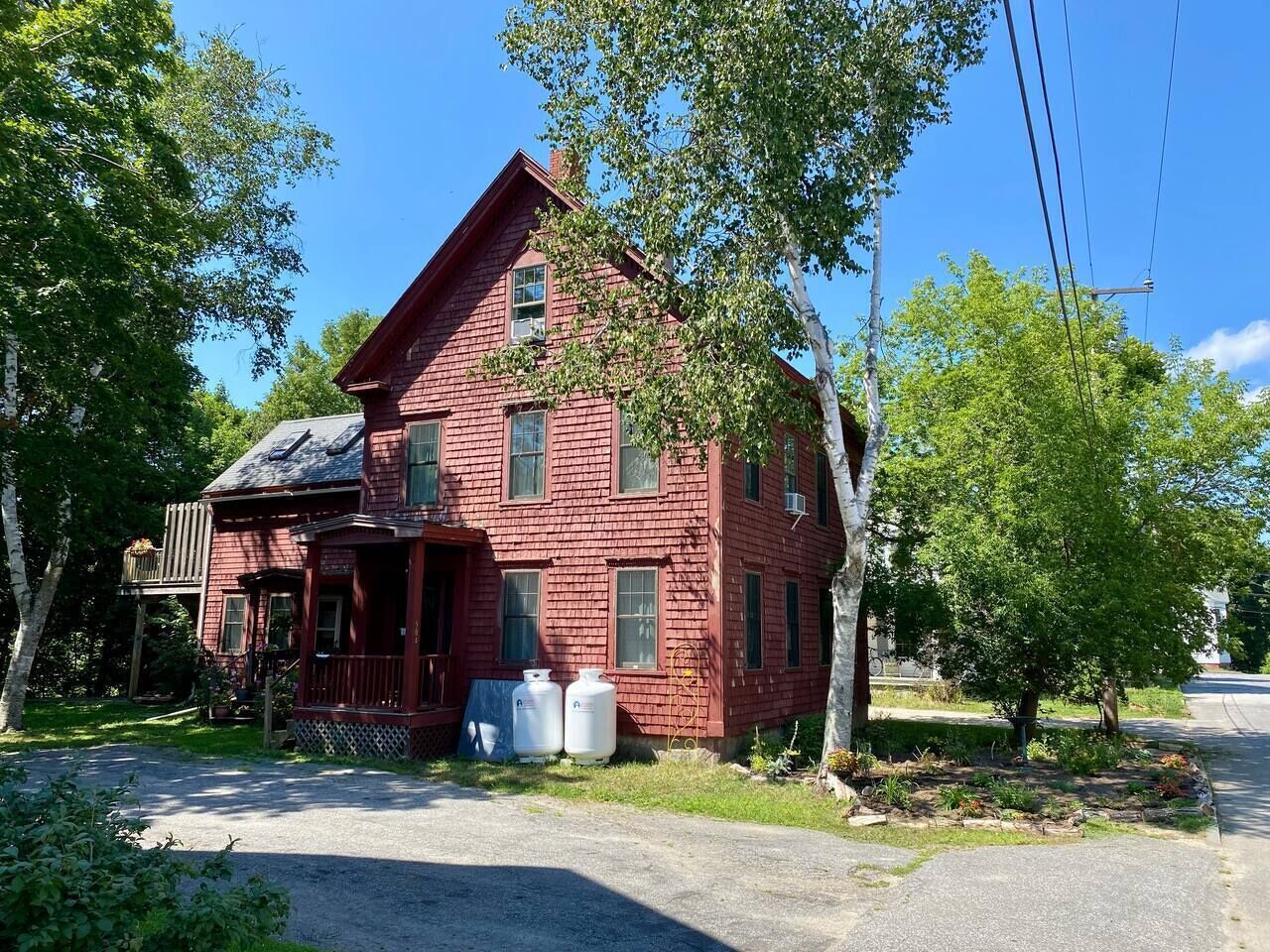 A red wooden house with a porch, two large white tanks, and a well-maintained garden.