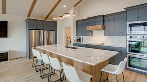 A modern kitchen with a large island, bar stools, stainless steel appliances, and a marble backsplash. - Breathtaking Views of Lake Texoma's beaches/Islands and Highport Marina.
 (Pottsboro)