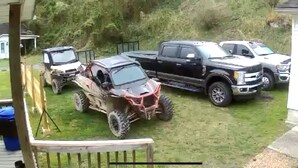 Zona residencial amb una casa, un balcó de fusta i tres vehicles aparcats a l'herba.