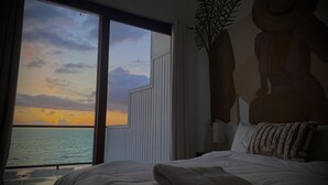 A hotel room with a large window overlooking a body of water during sunset.