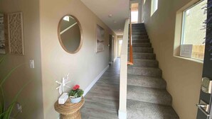 A hallway with a carpeted staircase, a round mirror, and a wicker basket with decorative items. - Modern Rooftop Zen with Ocean and Mountain Views (Grover Beach)