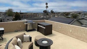 A rooftop patio with outdoor furniture, including a sofa and a round table, and a view of the surrounding neighborhood. - Modern Rooftop Zen with Ocean and Mountain Views (Grover Beach)