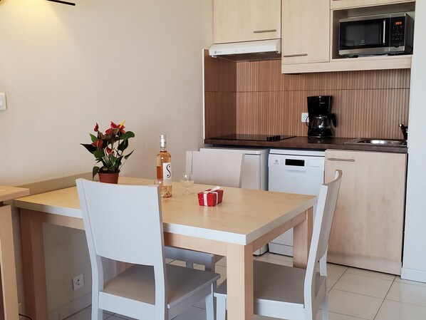 A compact kitchen with a microwave, coffee maker, and dishwasher. There is a dining table with chairs and a potted plant.