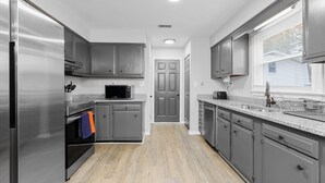 A modern kitchen with stainless steel appliances, grey cabinets, and a granite countertop. - The Full House (Chesapeake)