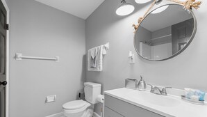 A bathroom with a toilet, a sink with a mirror, a towel rack, and a hand dryer. - The Full House (Chesapeake)