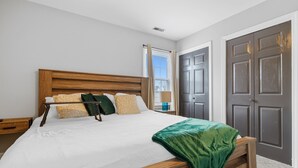 A bedroom with a wooden bed, white bedding, and a green throw blanket. - The Full House (Chesapeake)